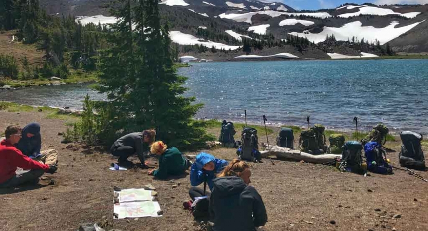 a group of students rest best an alpine lake on an outward bound course
